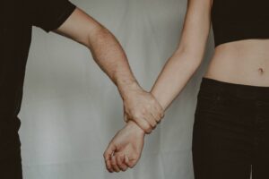 Unrecognizable aggressive man seizing hand of vulnerable helpless woman while standing on white background during domestic violence in light room